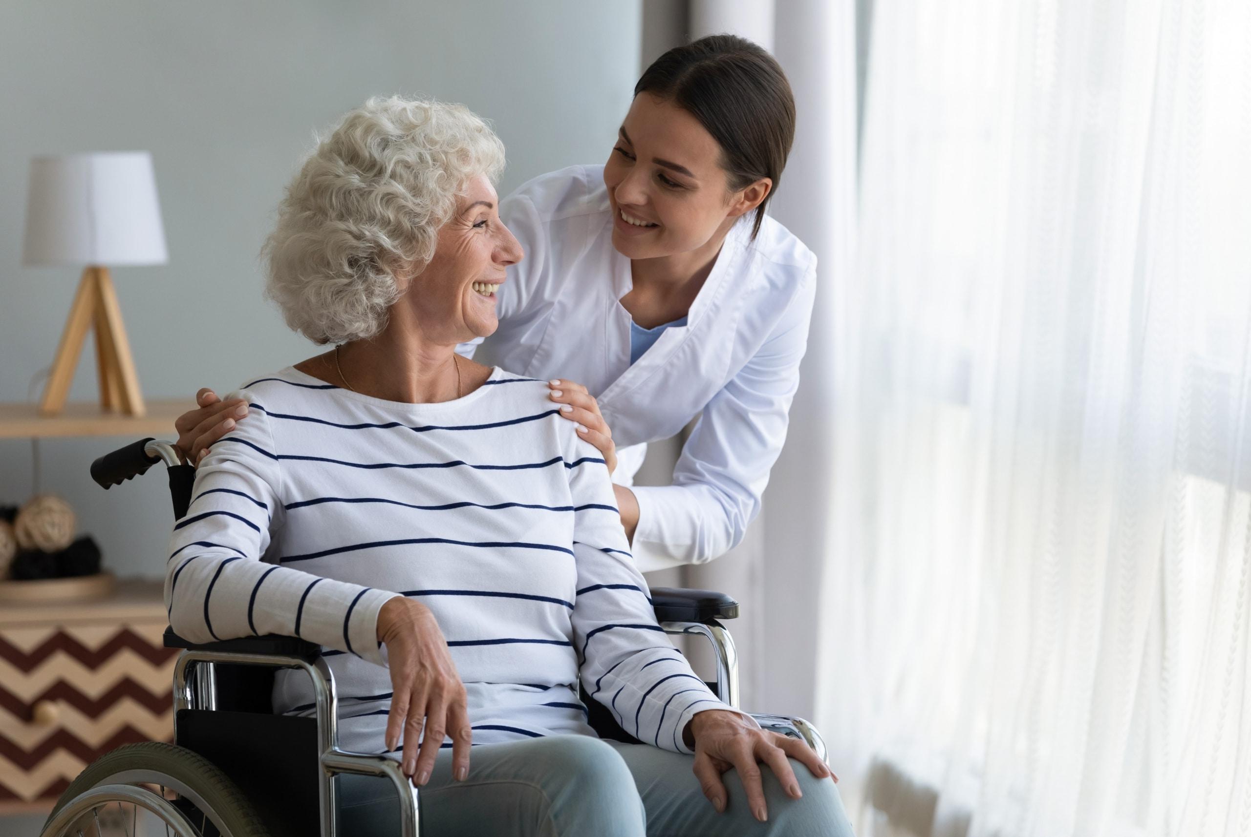 一位医疗专业人员对着一位坐在轮椅上的老妇人微笑